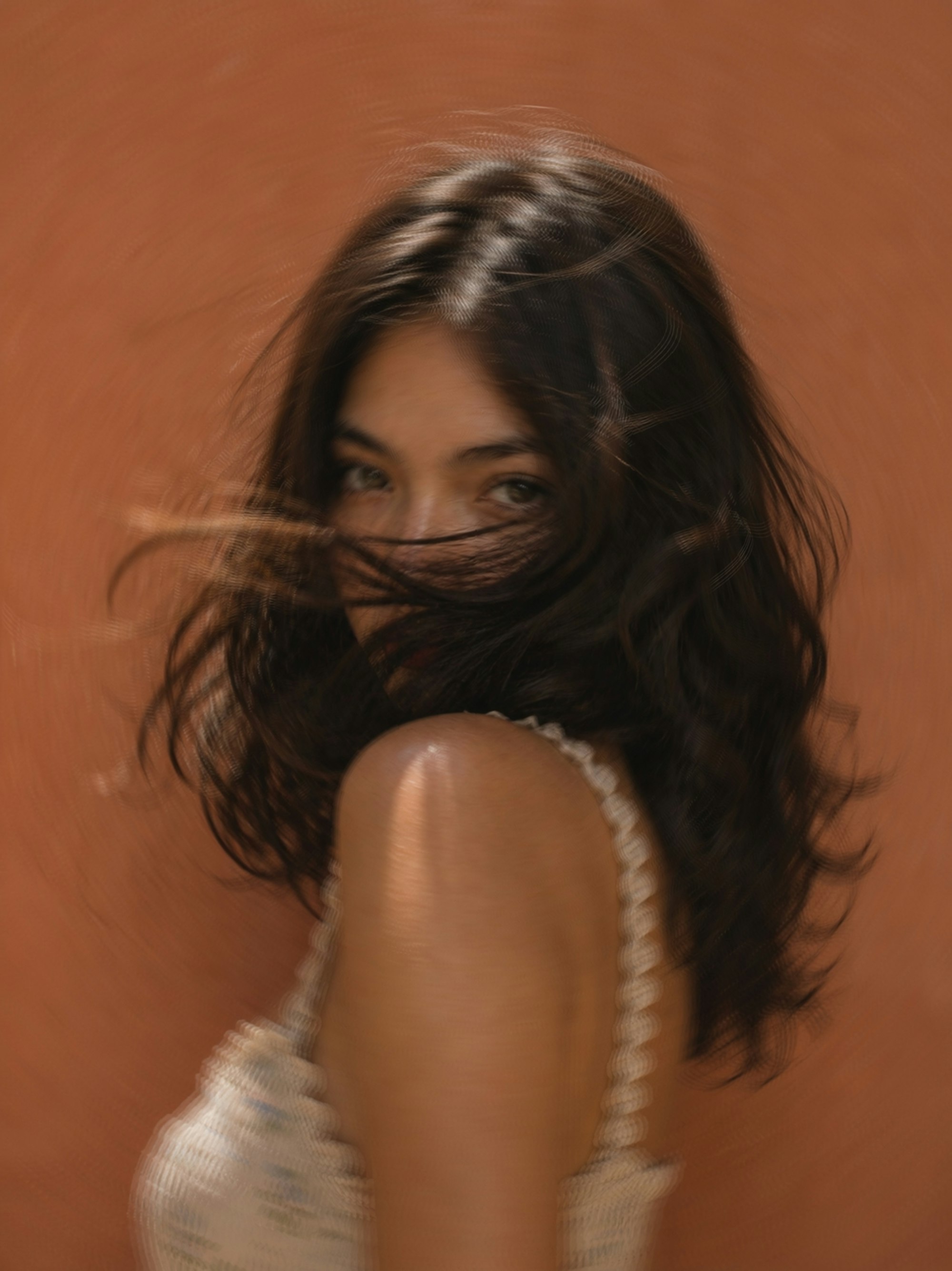 Woman with dark, softly layered wavy hair looking over her shoulder against a terracotta wall