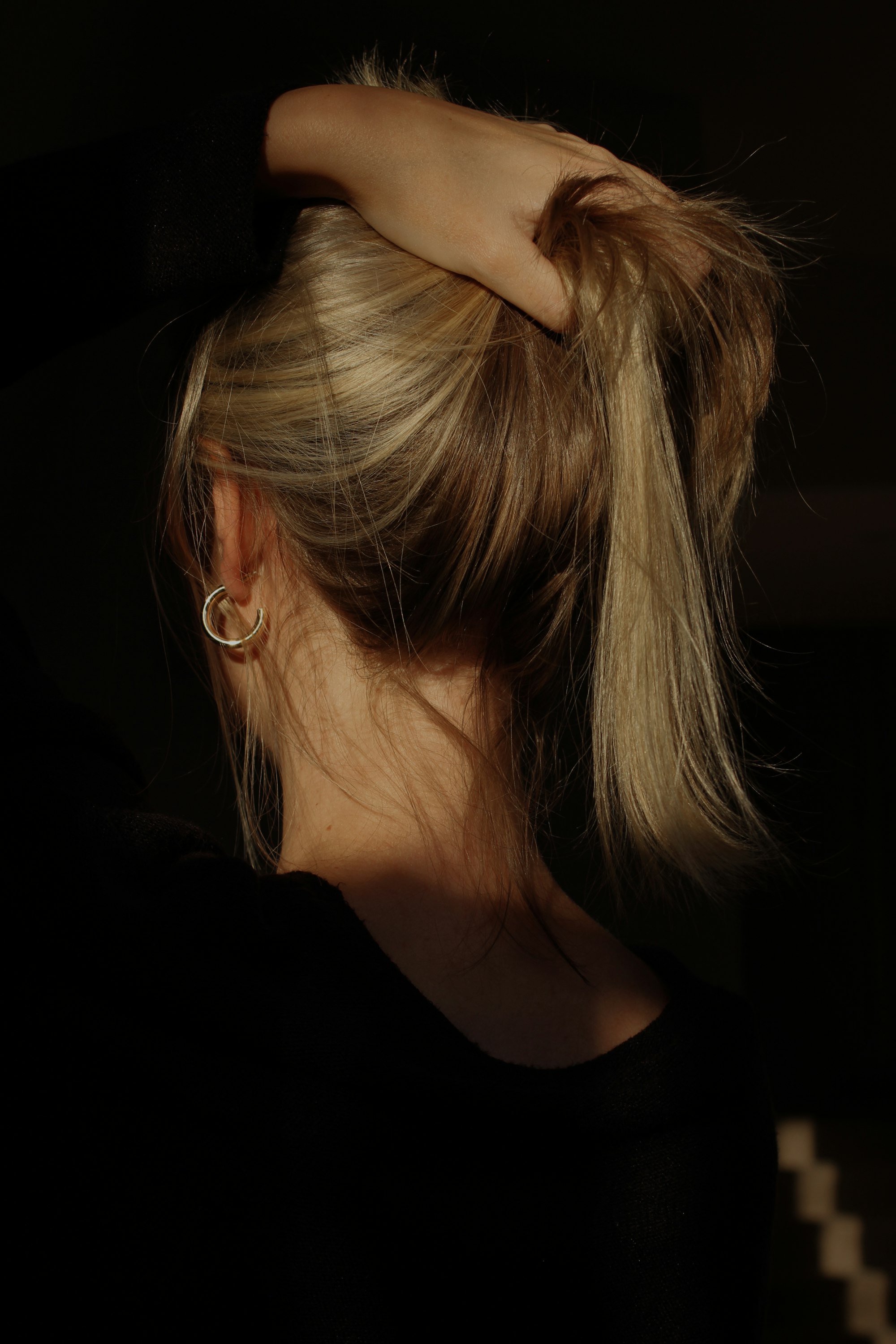 Woman with blonde hair gathered in a loose high ponytail, seen from behind