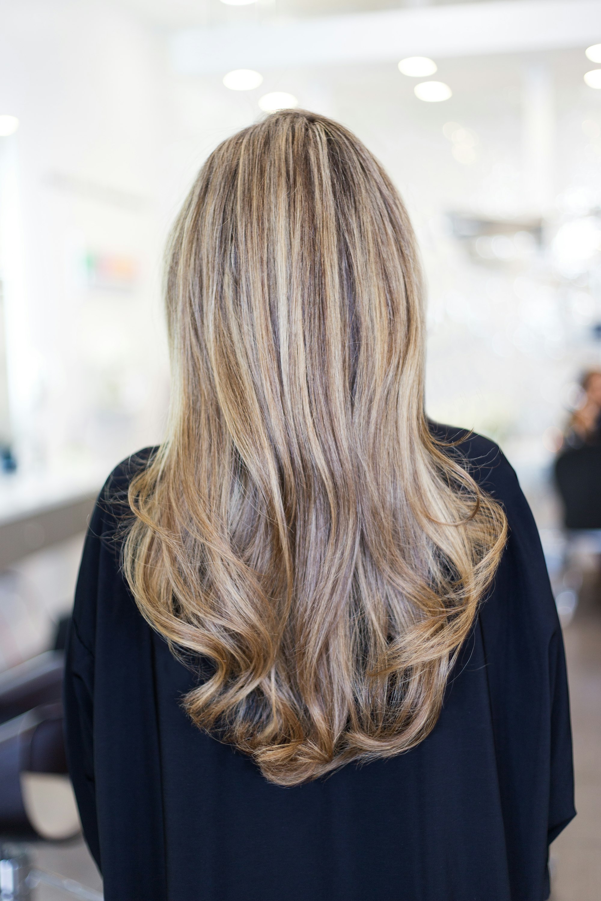 Long, healthy, softly highlighted hair falling down a woman's back in a bright salon
