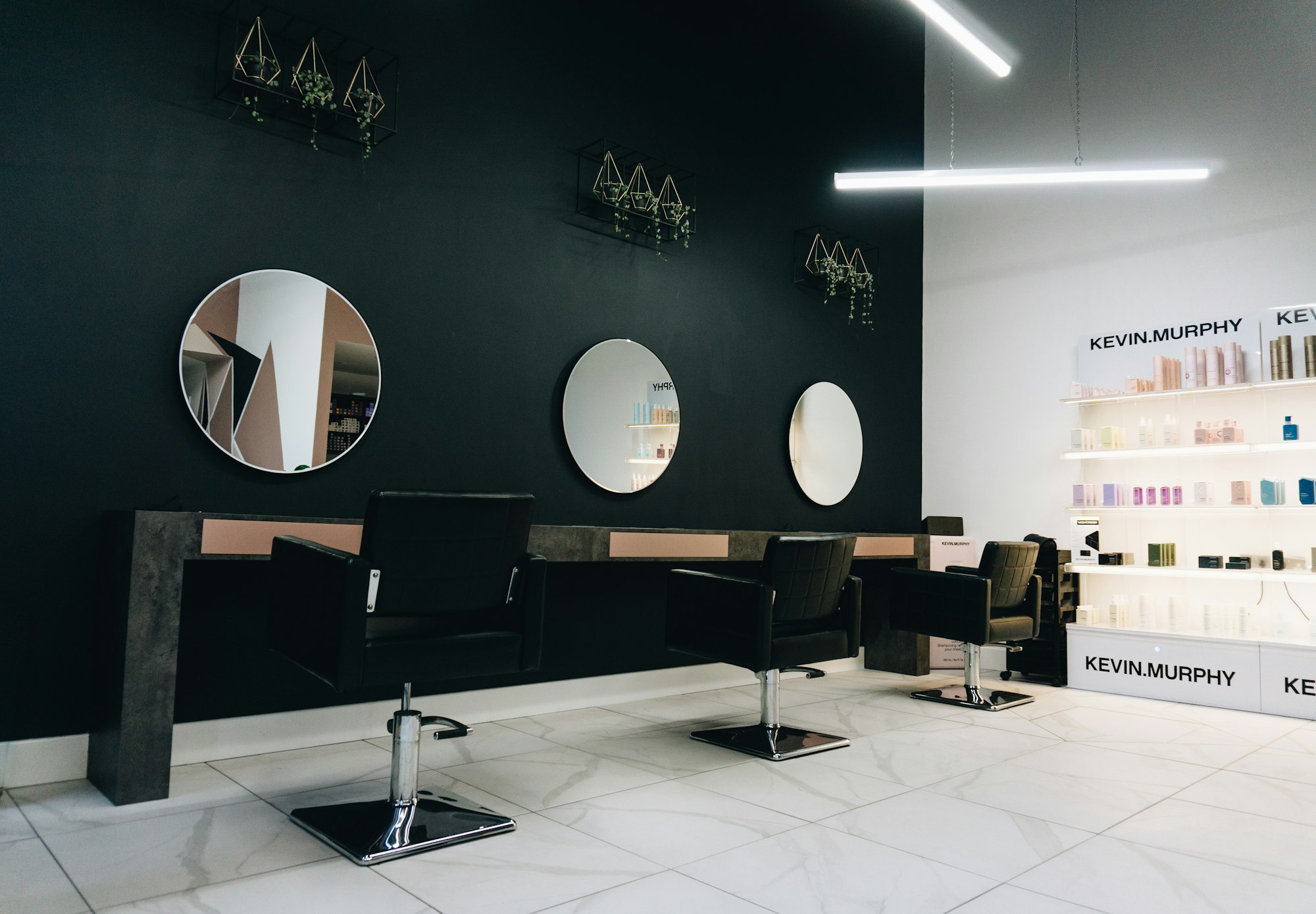 Three black salon chairs facing round mirrors on a dark wall