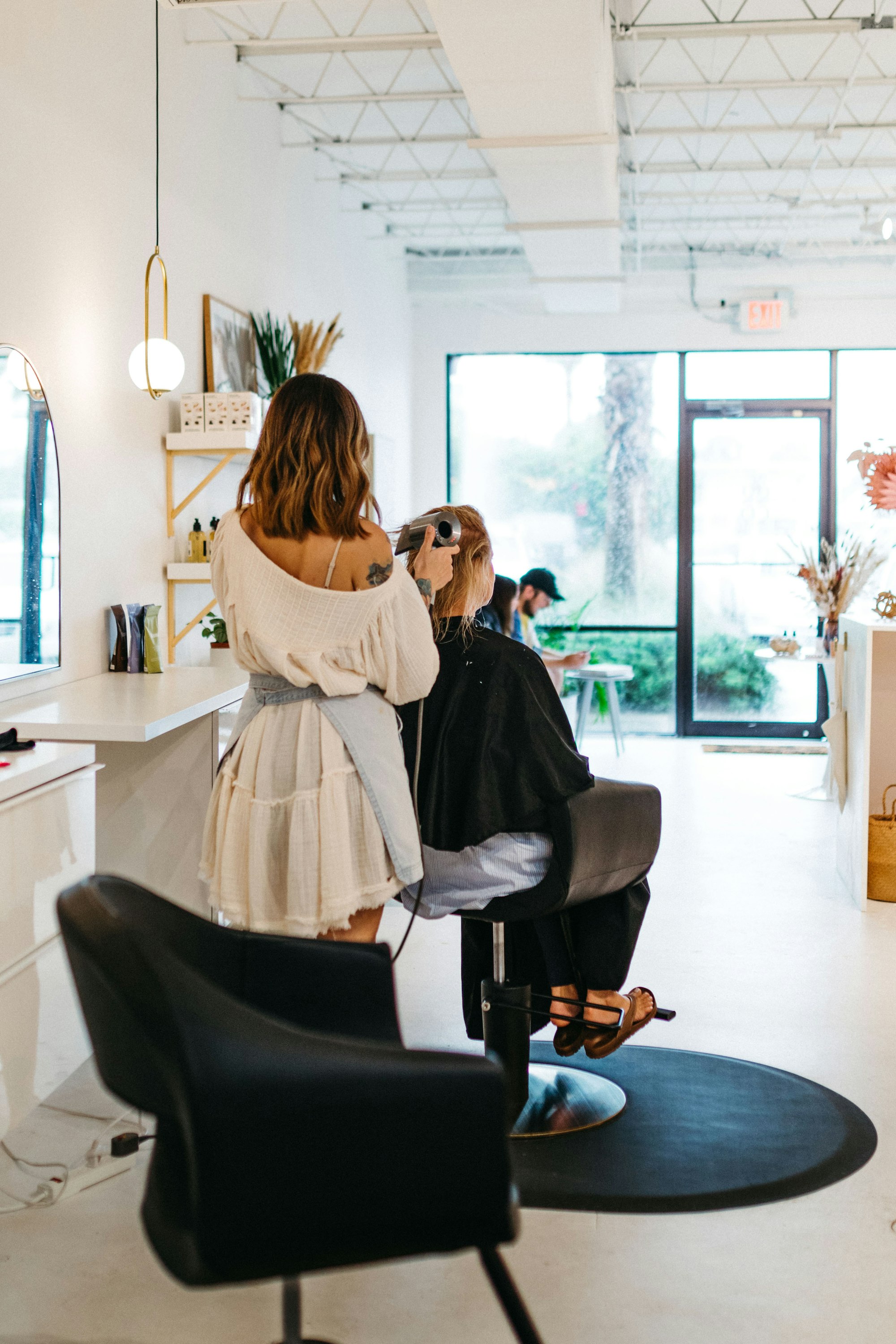 A stylist working on a client's hair at a bright salon station