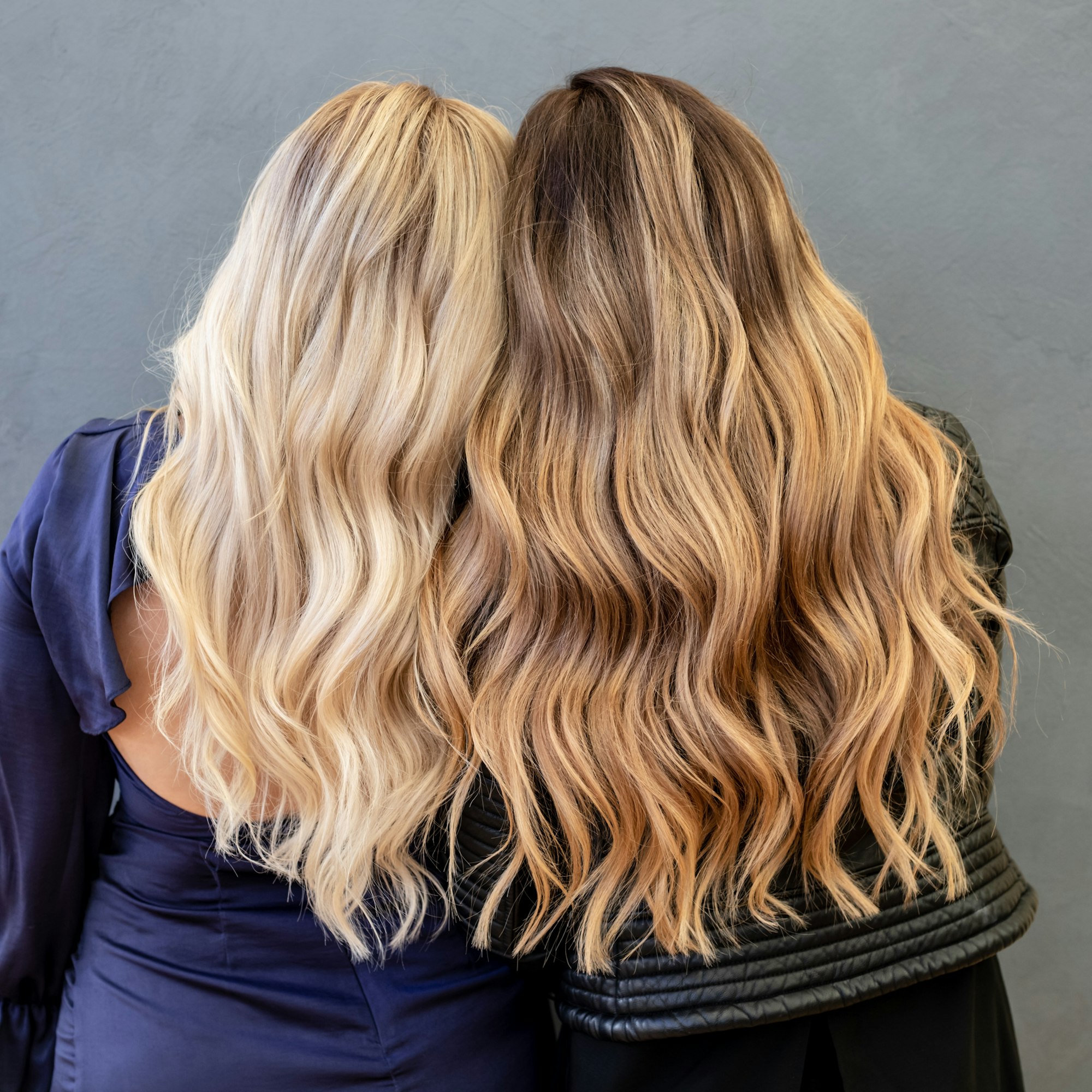 Two women with long wavy blonde and brunette balayage hair, seen from behind