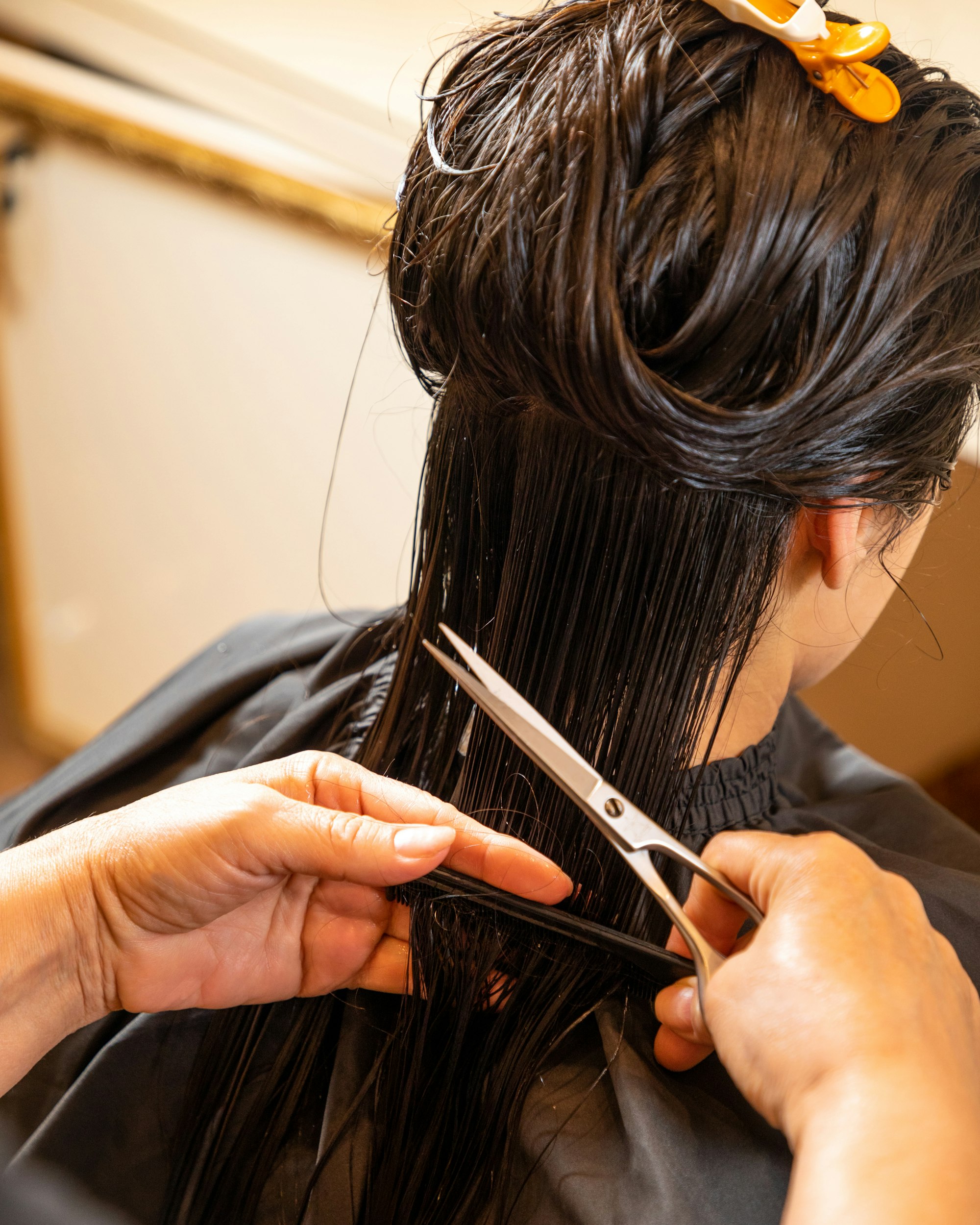 Hands cutting long dark hair with professional scissors