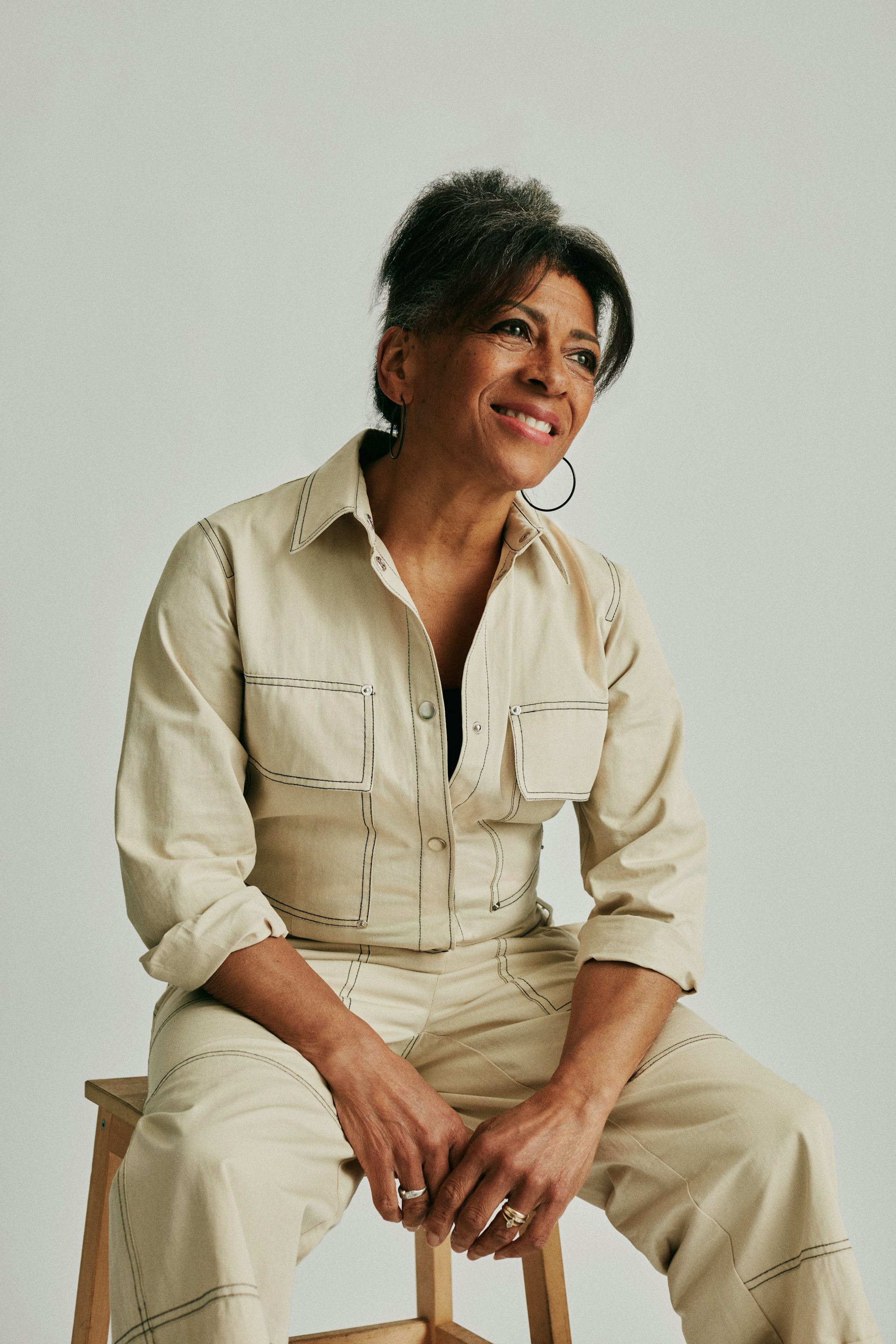 Smiling stylist in a beige jumpsuit seated on a stool